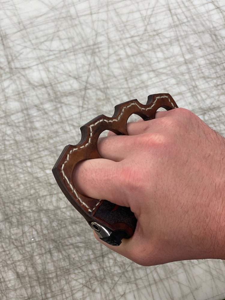 
                  
                    Hand wearing knuckle duster leather lighter; brown polished leather with cream stitching detail.
                  
                