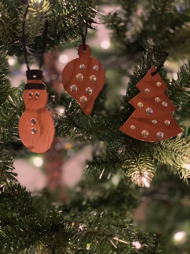 
                  
                    Three brown leather ornaments with rivets, hanging on Christmas Tree: Snowman, Christmas tree and classic ornament.
                  
                