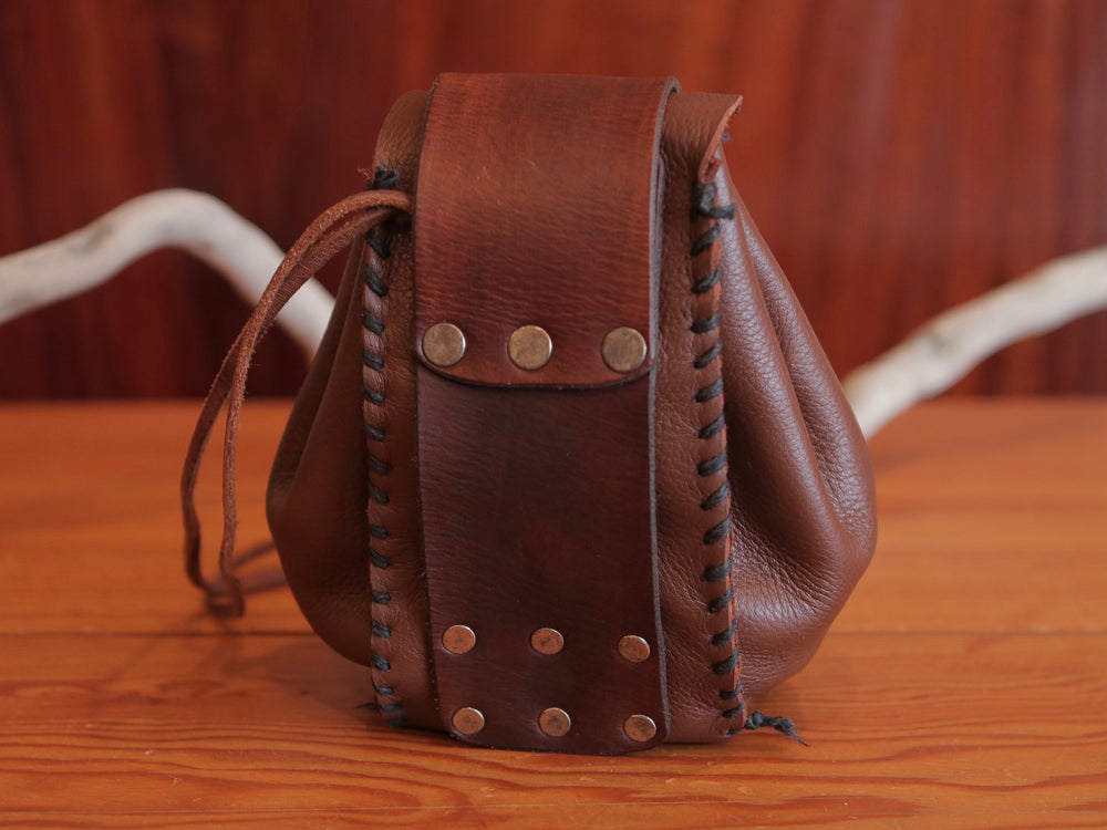 
                  
                    Back view of expandable brown leather handmade pouch, revealing belt holder, contrasting dark brown stitching, flat rivets and leather drawstring.
                  
                