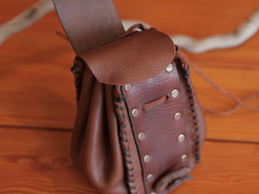 
                  
                    Top view of expandable brown leather handmade pouch, revealing second inner flap. Pouch has contrasting dark brown stitching, flat rivets, leather drawstring and rustic toggle to close at front.
                  
                