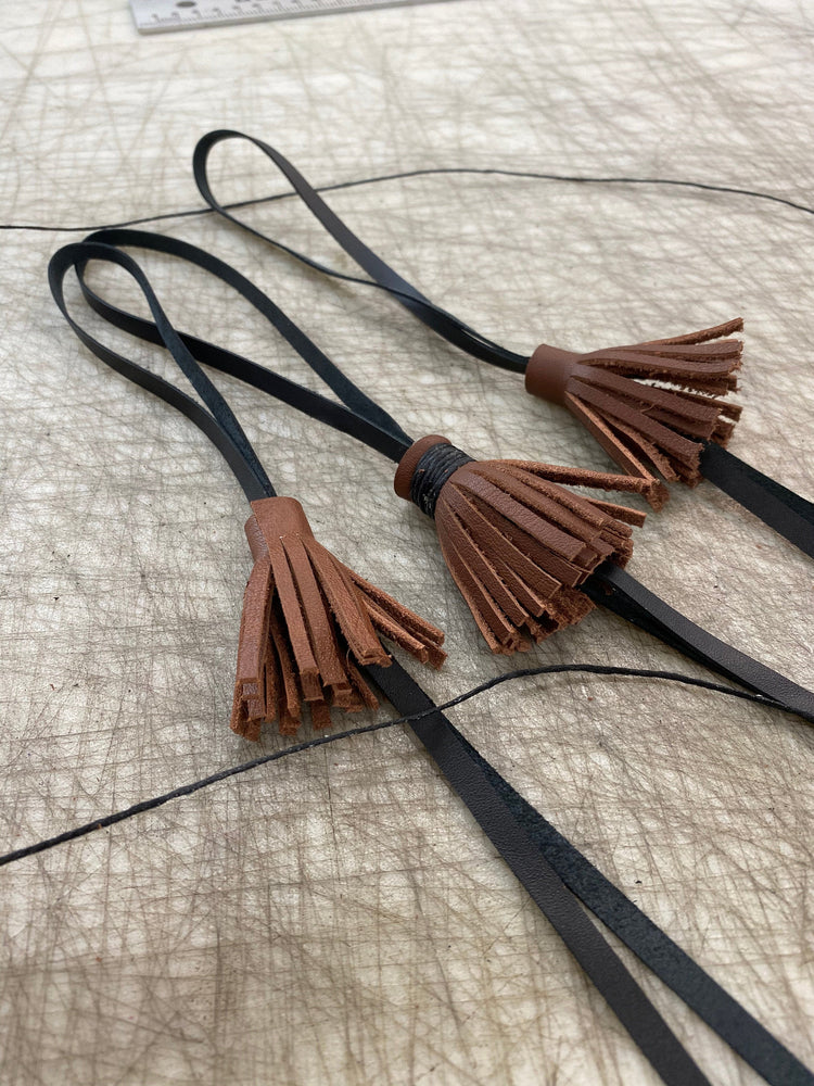 
                  
                    Detail of three brown leather handmade tassels with black leather attachments.
                  
                